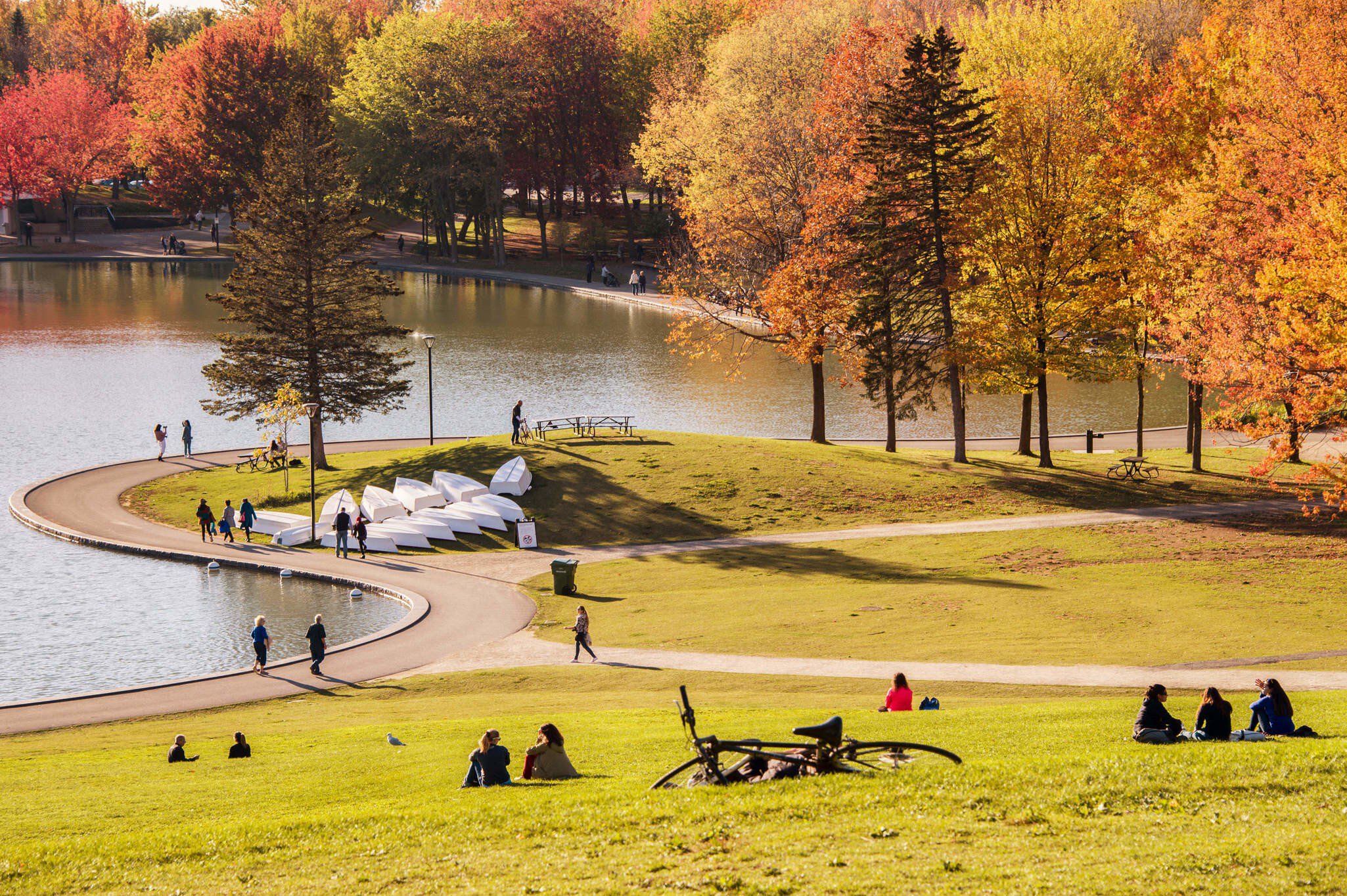 October 18, 2017: Visitors seated on the grass around a lake in Mont Royal Park during autumn.