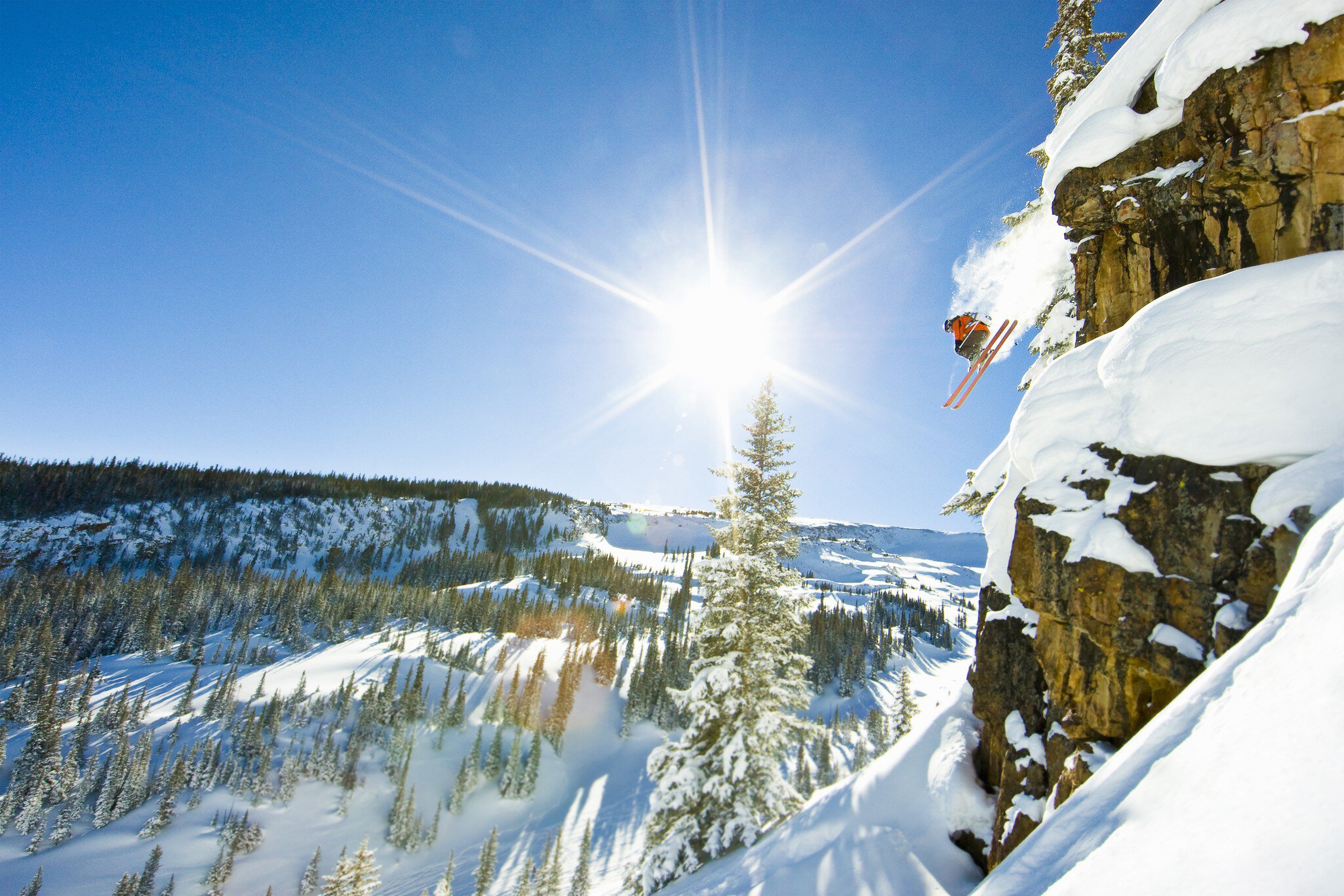 Skier jumping cliff on sunny winter day.