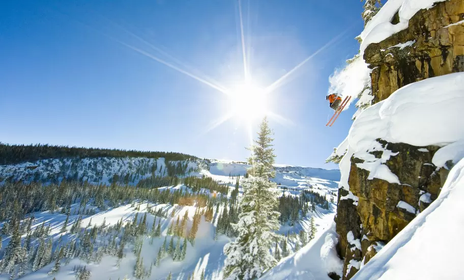Skier jumping off a cliff on sunny winter day in Aspen, Colorado.