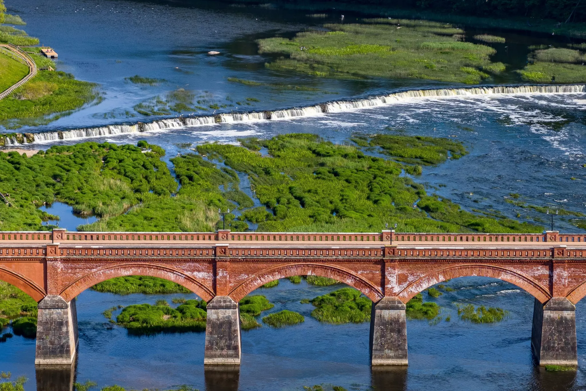 A brick bridge frames the famous waterfall at Kuldīga, Latvia.