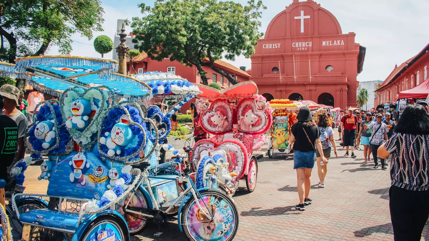 A row of colorful four-wheel cycles stand in a main square backed by a large church building painted red