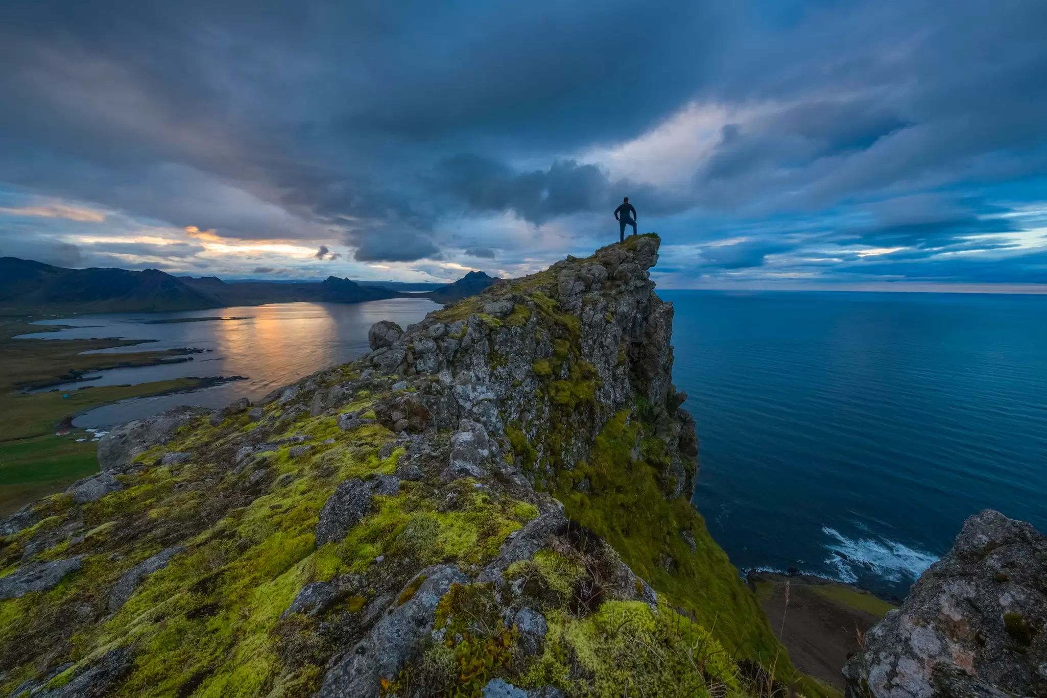A man stands atop a hill looking out at the waters around the Strandir coast, Iceland