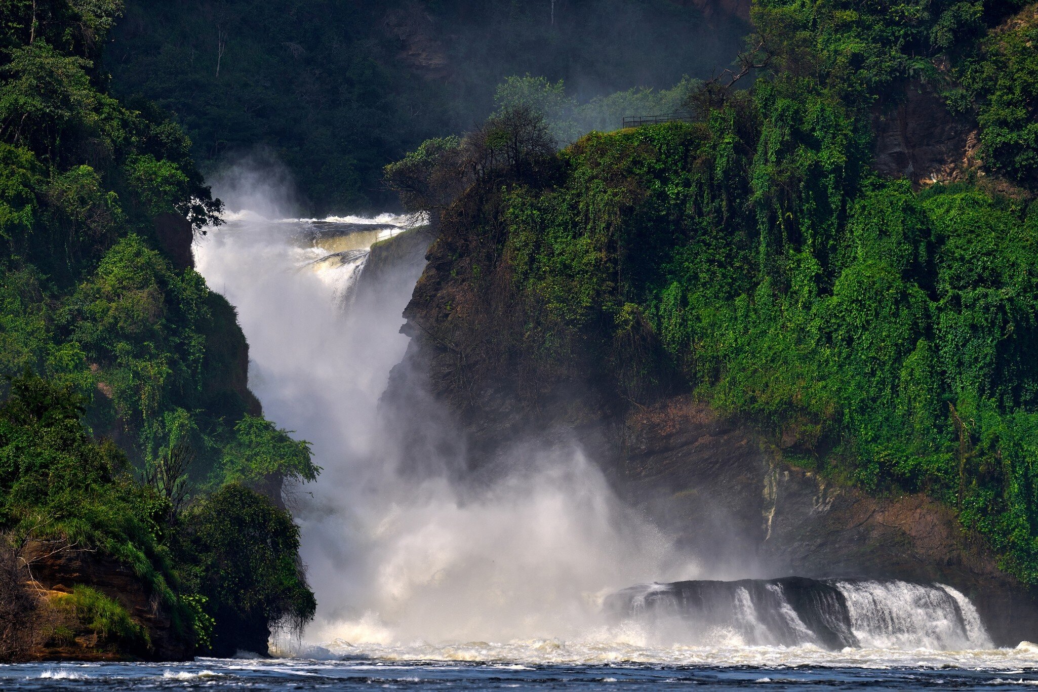 Murchison Falls, Uganda: white water plunging through a narrow rock gorge in a cloud of spray, forested cliffs at right
