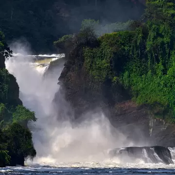 Murchison Falls, Uganda: white water plunging through a narrow rock gorge in a cloud of spray, forested cliffs at right