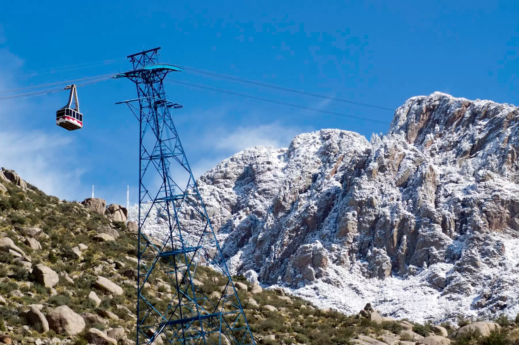 A gondola car at Sandia Peak Tramway passes a tower in front of a snow-capped mountain during winter. 
184883248
Extreme Terrain, No People, Landscape, Cable Car, Sandia Peak, Mountain Ridge, Beauty In Nature, Tourism, Mode of Transport, Travel Destinations, Horizontal, Mountain Peak, Contrasts, Blue, Transportation, Photography, Travel, Scenics - Nature, Sandia Mountains, Outdoors, Nature, Ski Lift, Mountain, Winter, Tower, Landscape - Scenery, Overhead Cable Car, In Front Of, Ridge, Environment