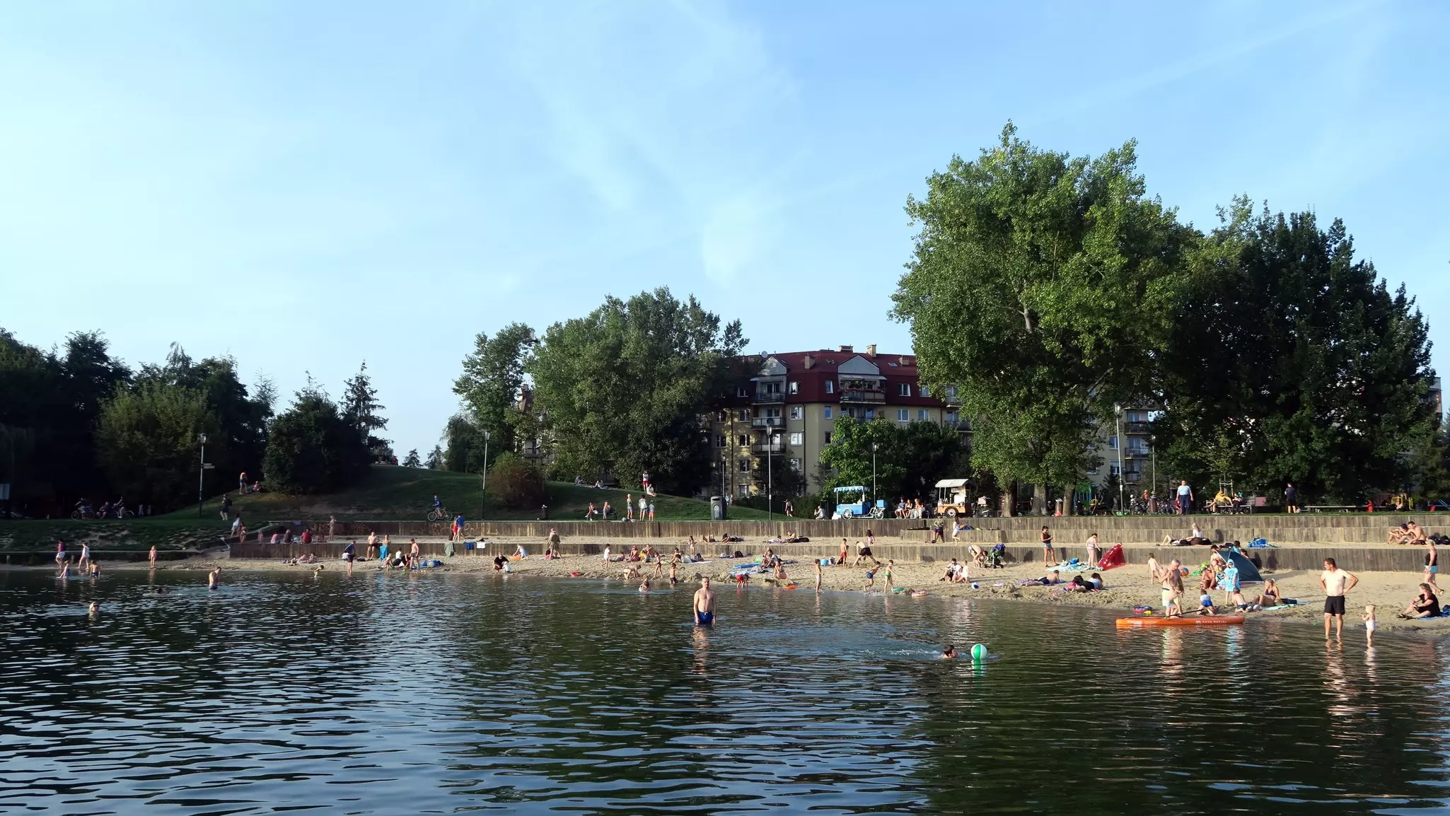 People wading in water and sunbathing on a beach at a lake in Kraków.