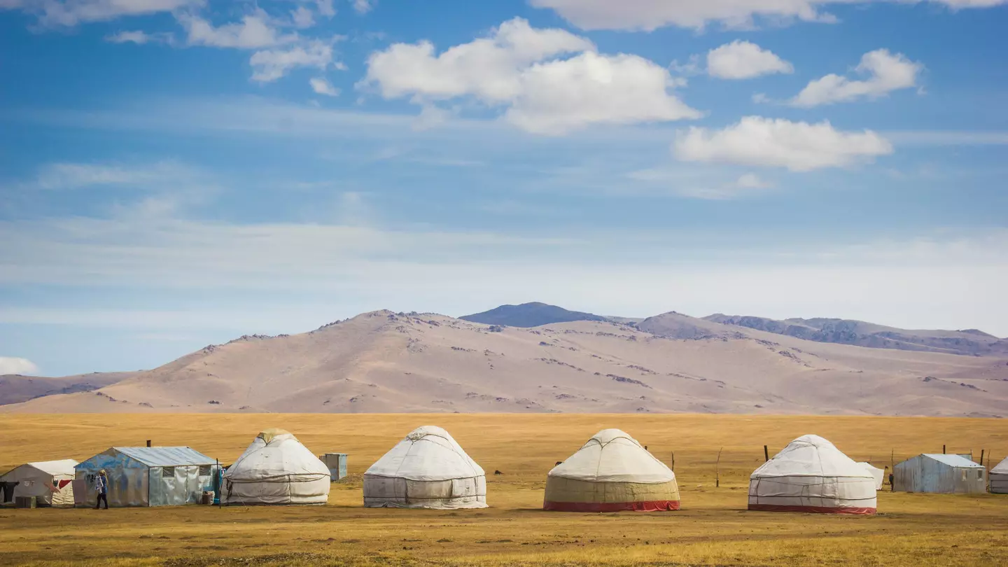 Mountains are foregrounded by yurts in a meadow near Song Kol Lake, Kyrgystan.