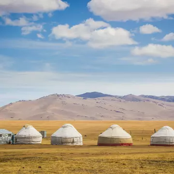 Mountains are foregrounded by yurts in a meadow near Song Kol Lake, Kyrgystan.