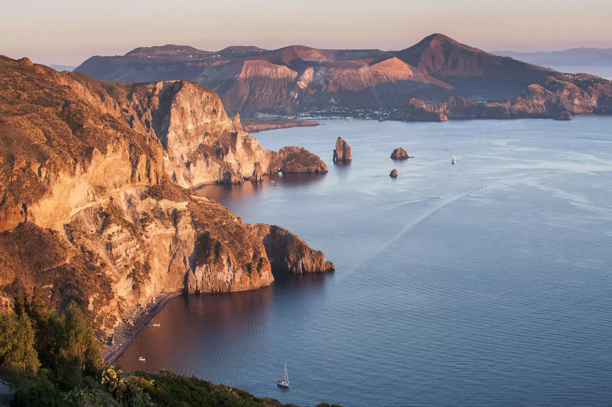 A volcanic coastline of cliffs with boats sailing by.