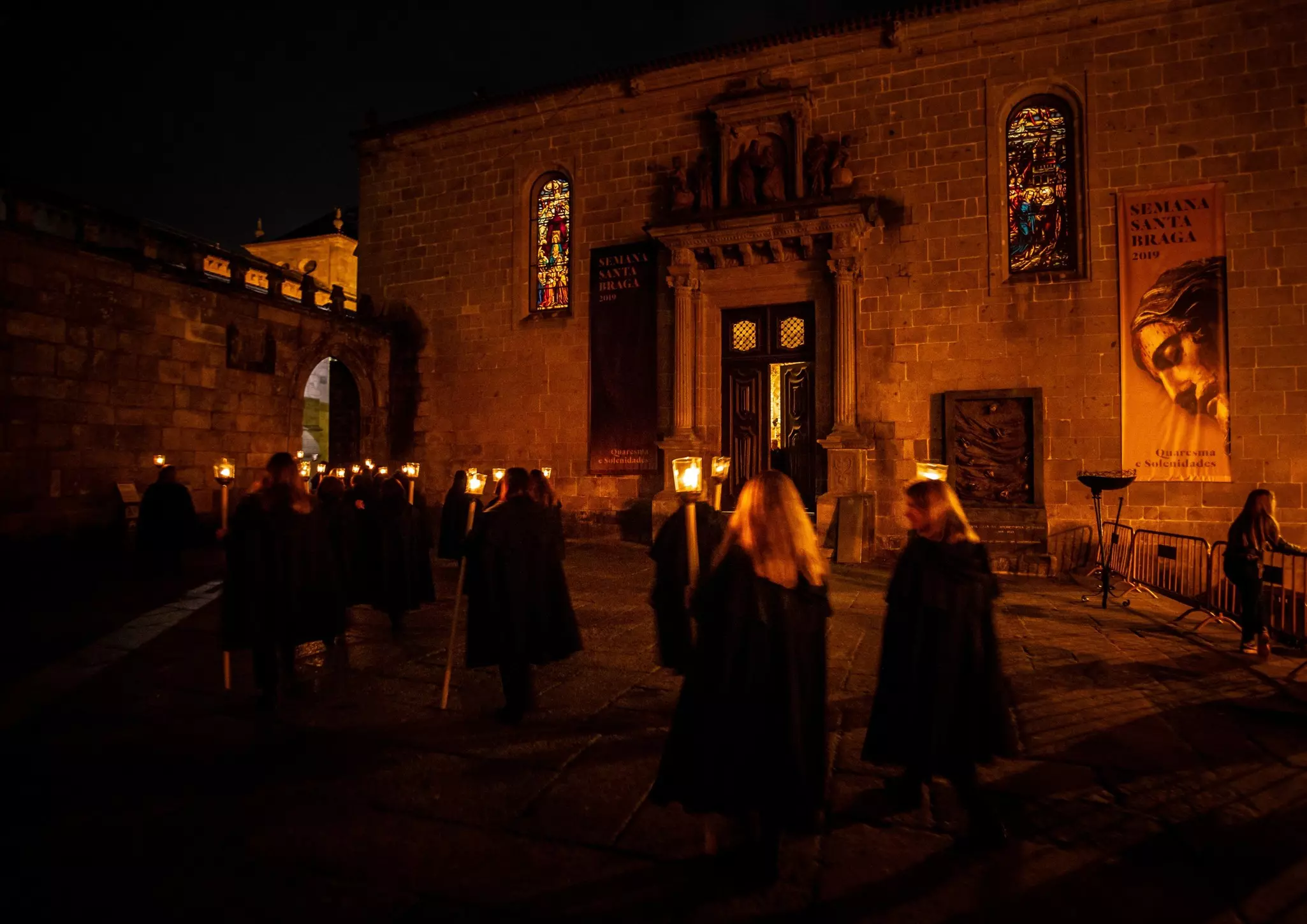 People in hooded robes carry torches down a city street during a nighttime religious procession in Portugal.