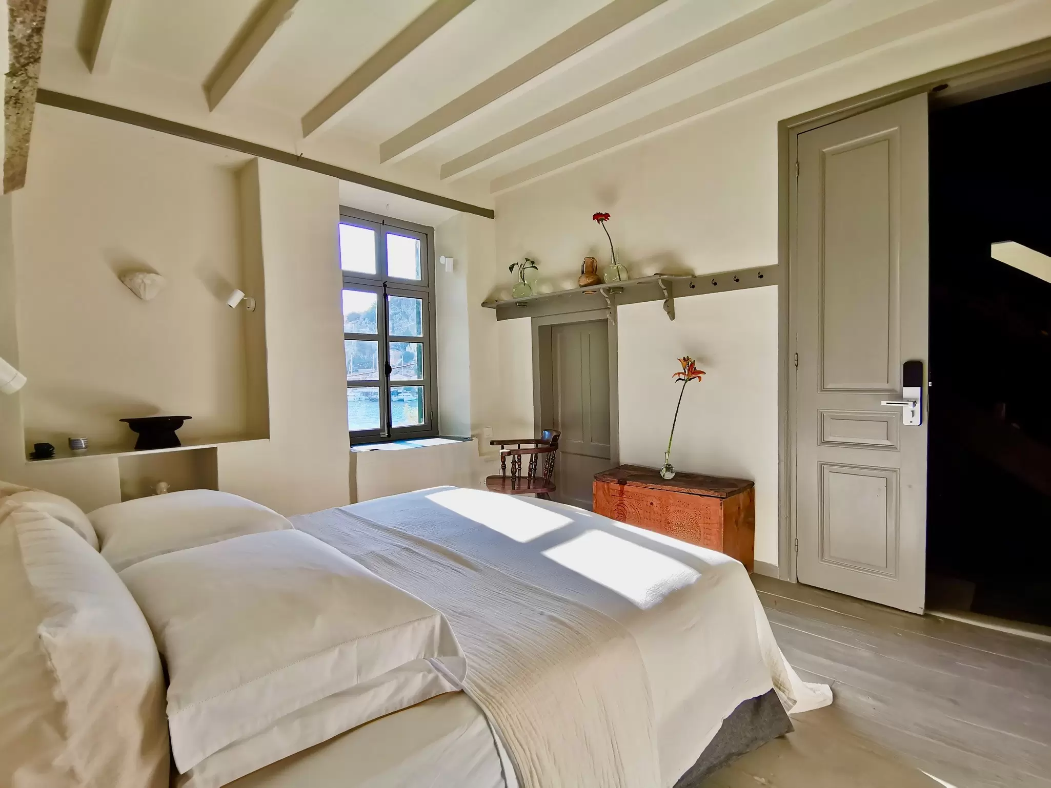 A quaint room with a sun-lit window and a view out towards a harbor: Room 1902 at 1900 Hotel, Symi, Greece.