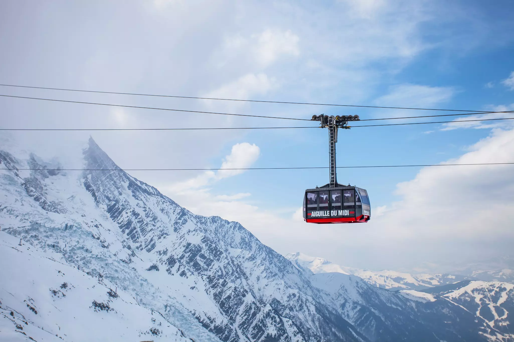 A large gondola travels on cables over snowy mountain slopes.
