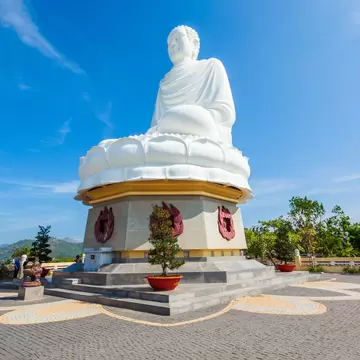 Long Son Pagoda, Nha Trang: white seated Buddha on a lotus base above a plinth with red flame reliefs, hills behind