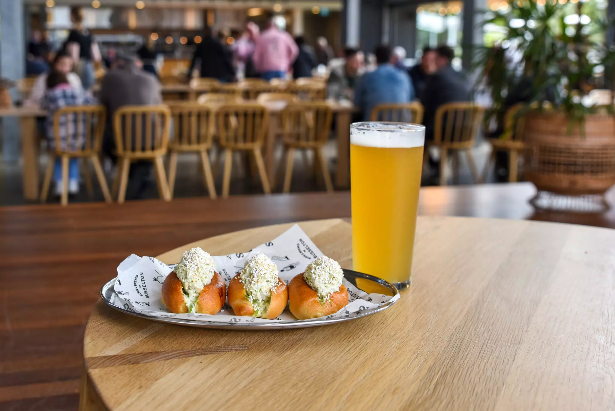 A pint of cold beer on a table near three small subway sandwiches in a pub.