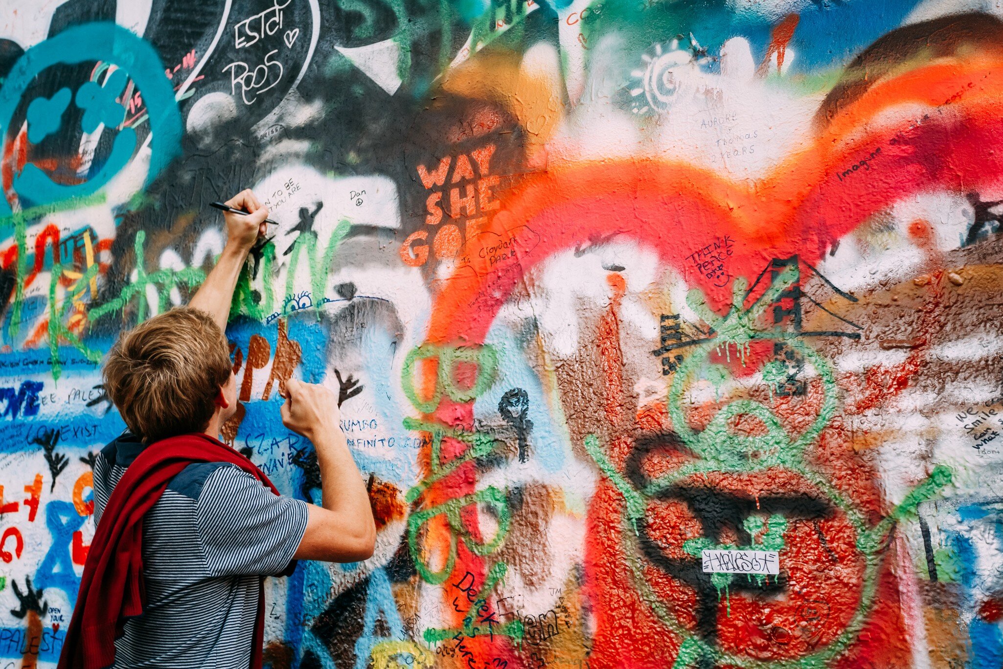 Prague, Czech Republic. Person draws on the John Lennon Peace Wall. Wall filled with Lennon inspired graffiti and lyrics from Beatles songs. 
