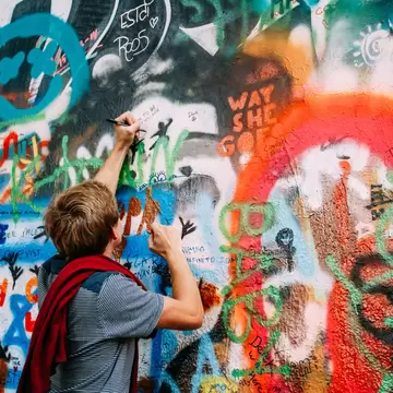 Prague, Czech Republic. Person draws on the John Lennon Peace Wall. Wall filled with Lennon inspired graffiti and lyrics from Beatles songs. 