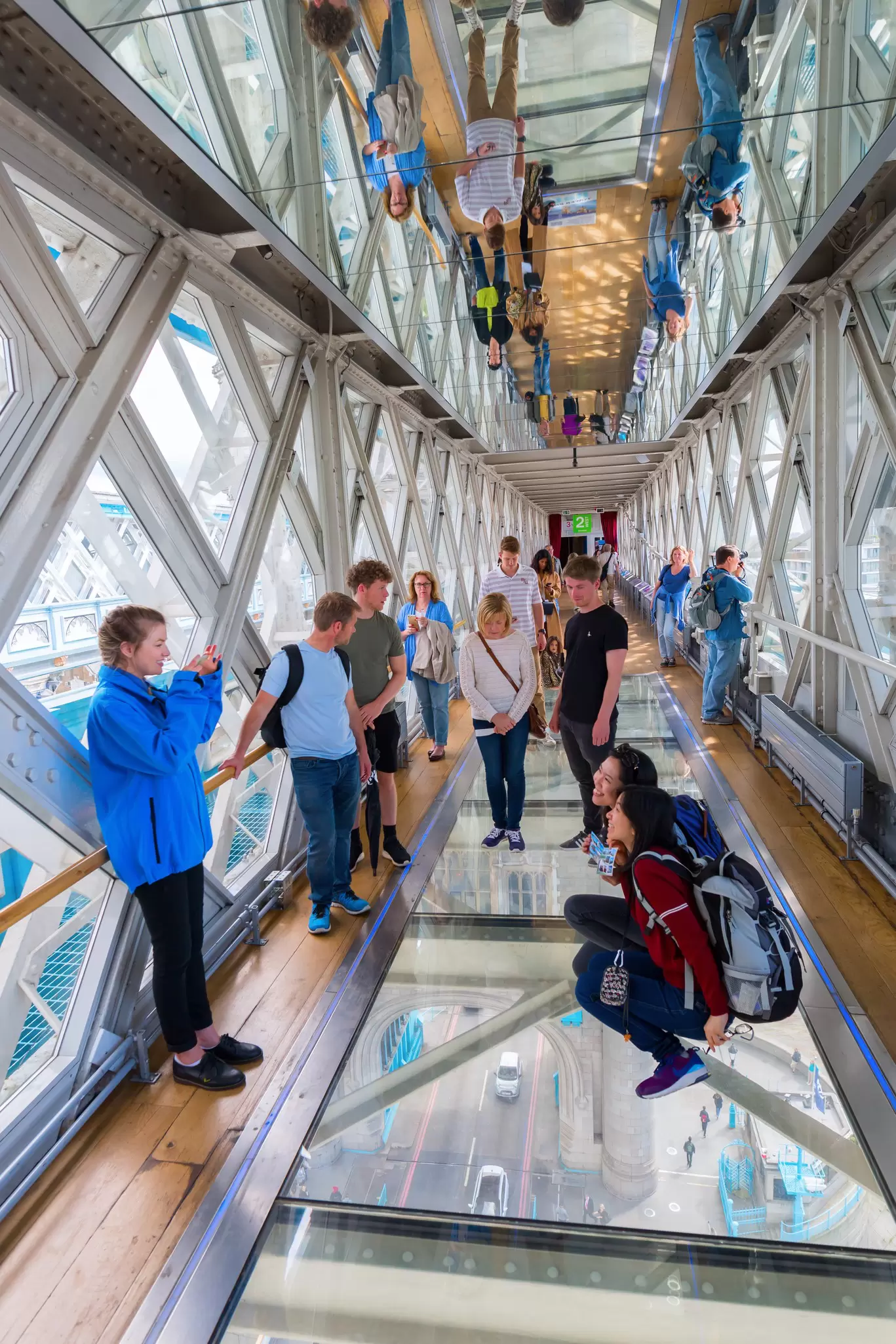 A group of people standing on a glass walkway high above a road pose for photos