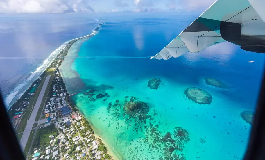 Aerial view of Funafuti atoll in Tuvalu from a plane window: airstrip, houses on a thin strip of land and a turquoise lagoon