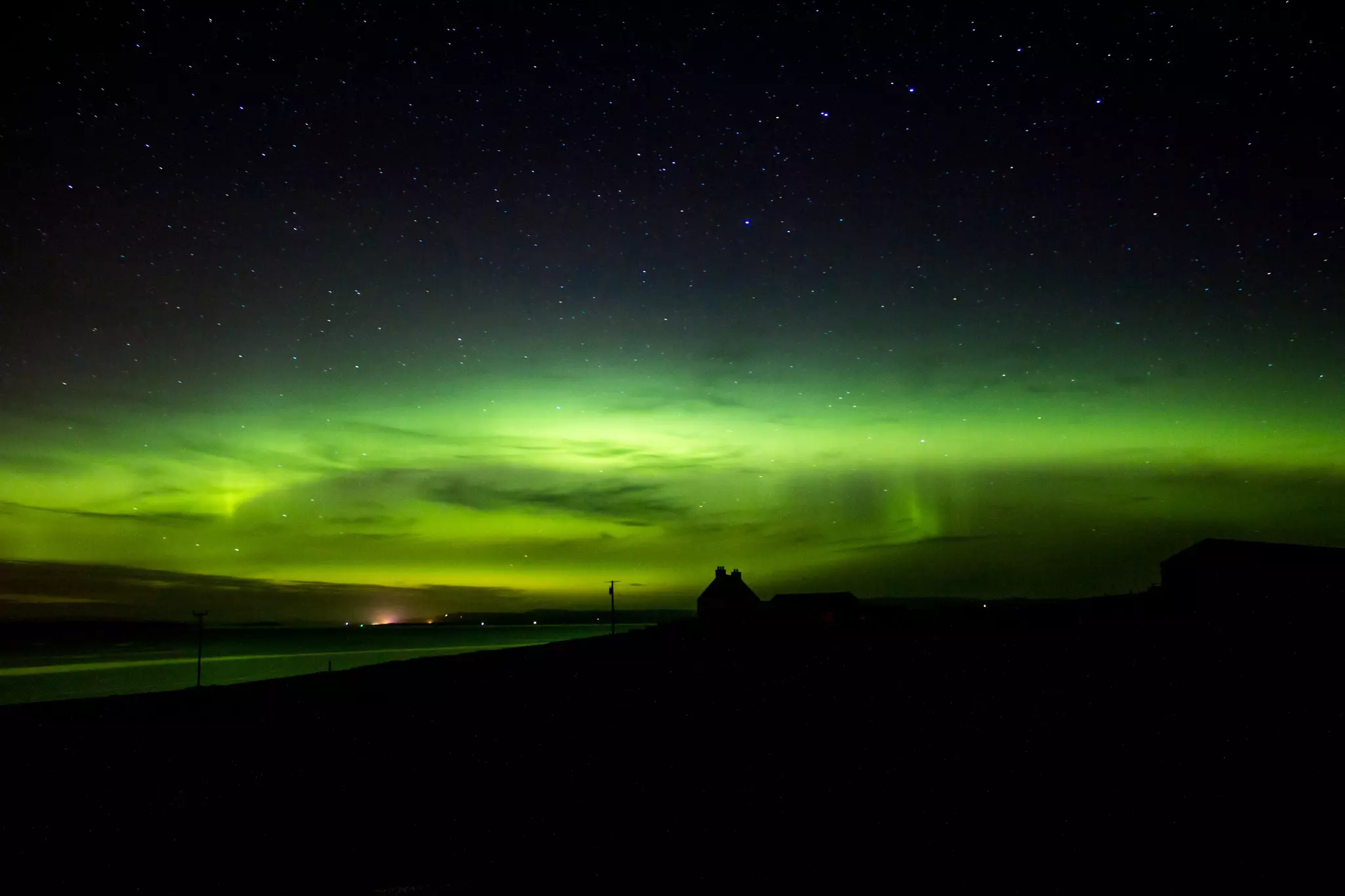 Green lights from the aurora borealis in a dark sky with a building silhouetted in front.