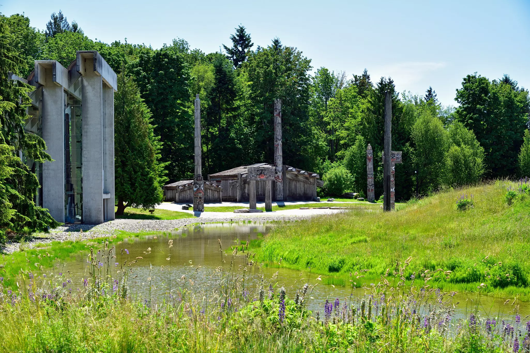 A series of carved wooden poles and small structures near a stream on a summer's day.