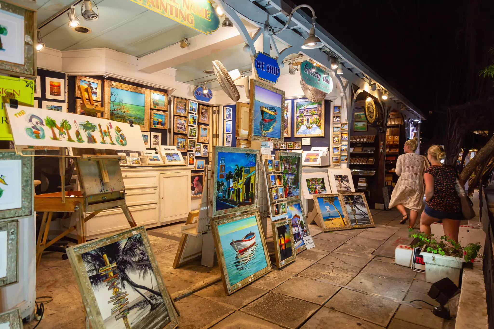 Paintings and other artwork are for sale at a stall on a street at night.