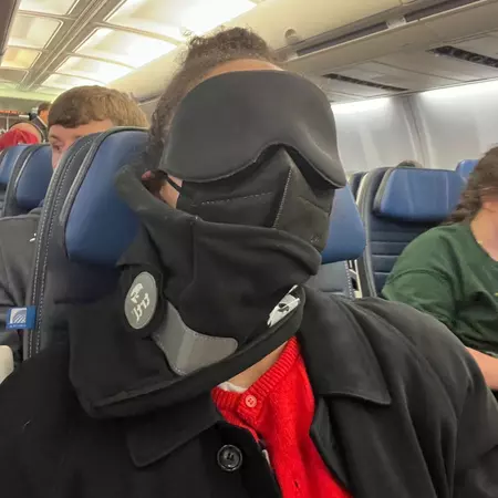 A woman wearing a sleep mask and travel pillow on a plane