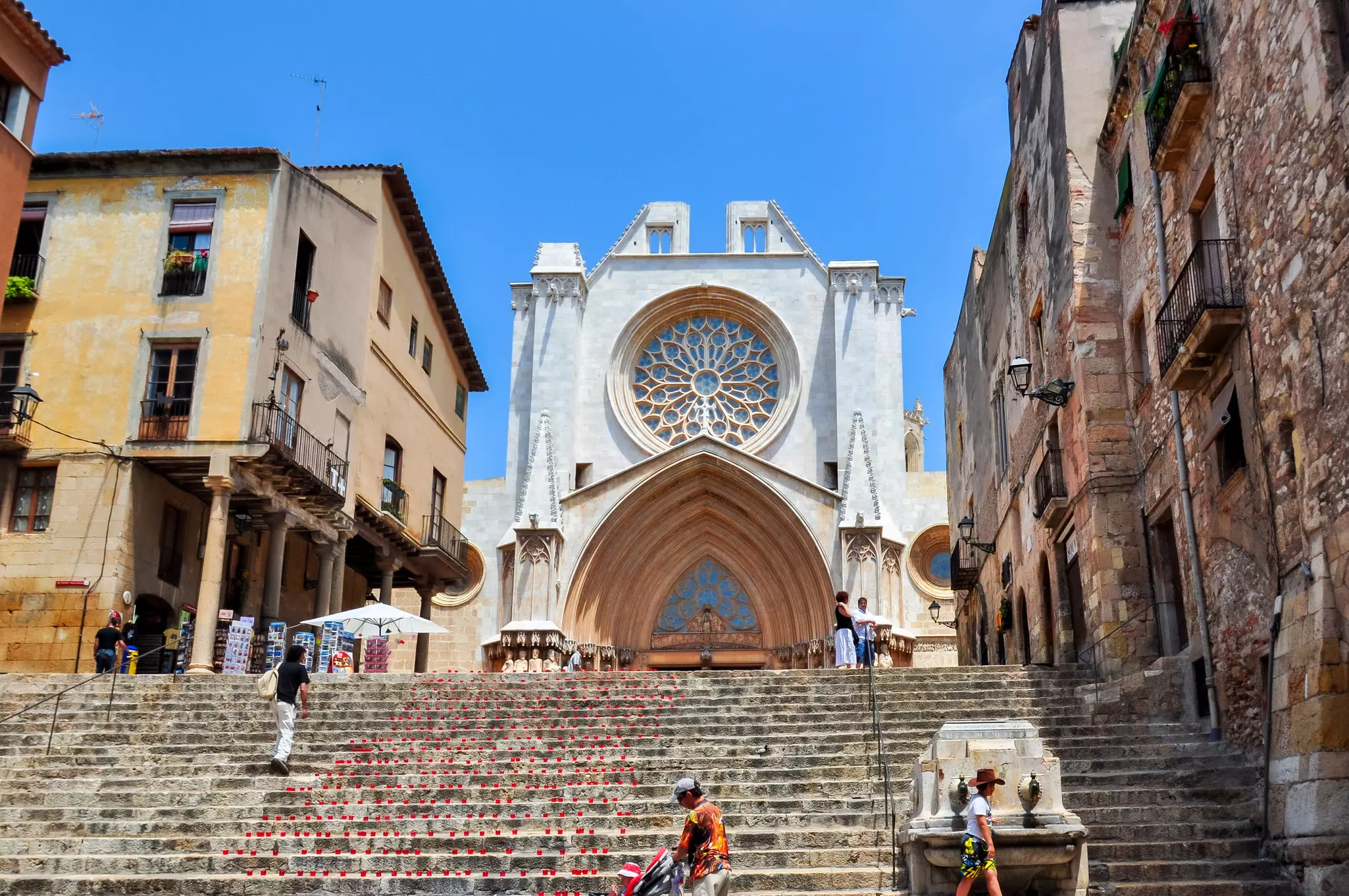 Looking up at the Tarragona Cathedral (Catedral de Tarragona) facade from steps below it with pedestrians passing.
