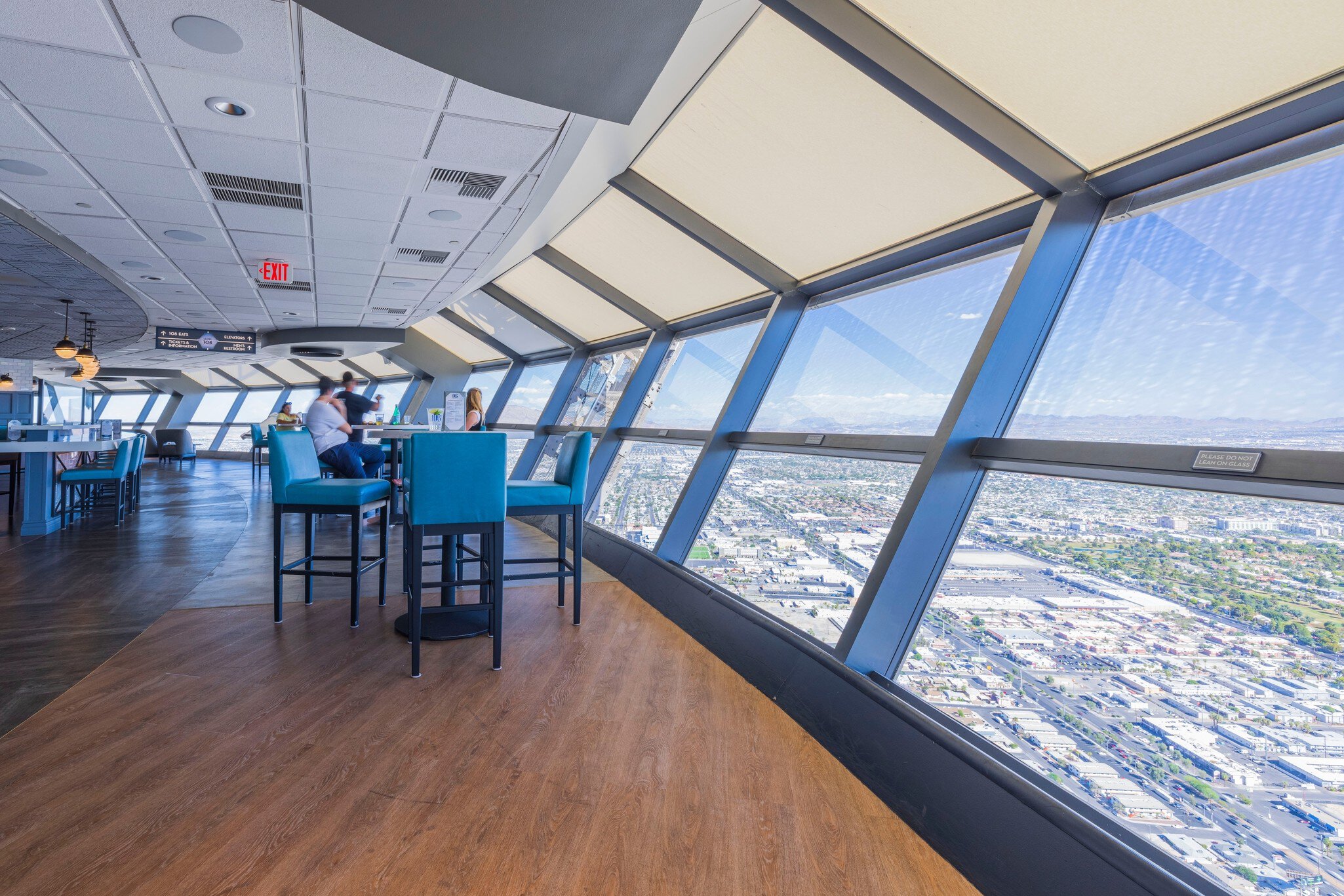 Teal bar stools at high tables beside angled windows overlooking a city far below.