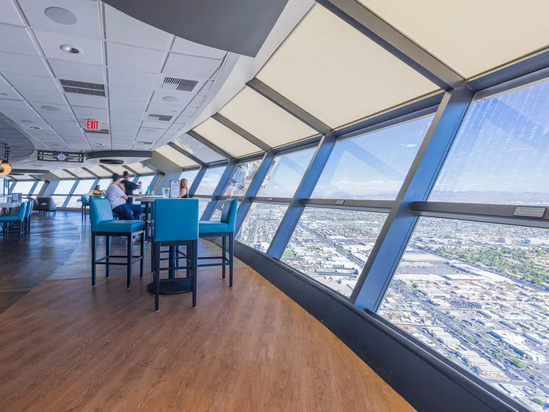 Teal bar stools at high tables beside angled windows overlooking a city far below.