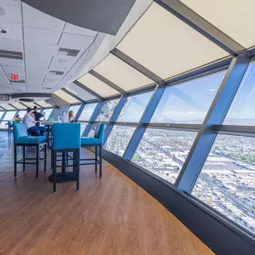Teal bar stools at high tables beside angled windows overlooking a city far below.