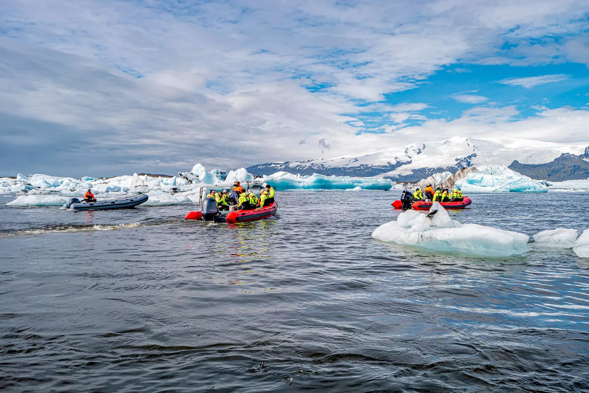 Rigid inflatable boats ply a glacial lagoon with many small icebergs.