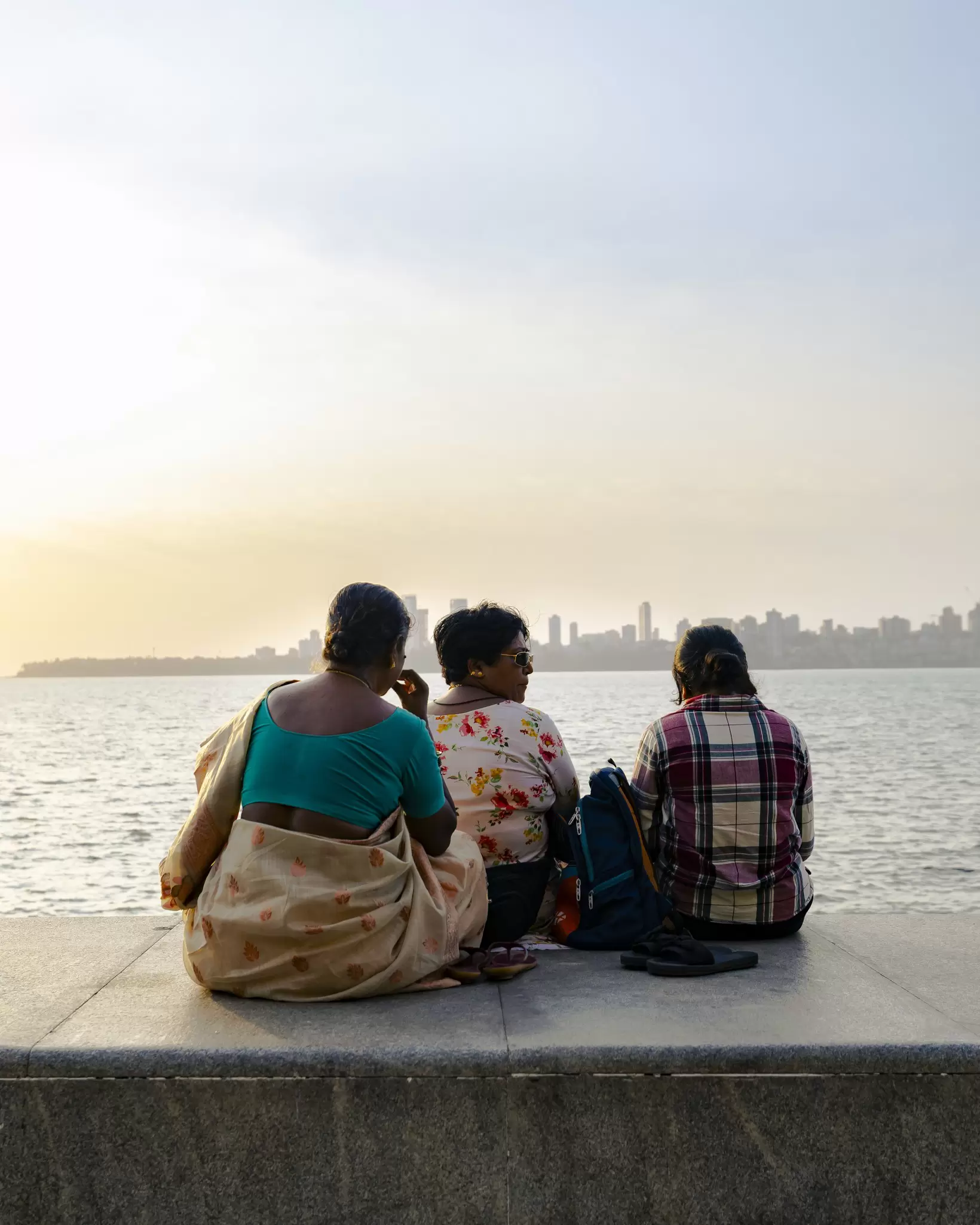 Three women sit looking at the water along Marine Drive, Mumbai.