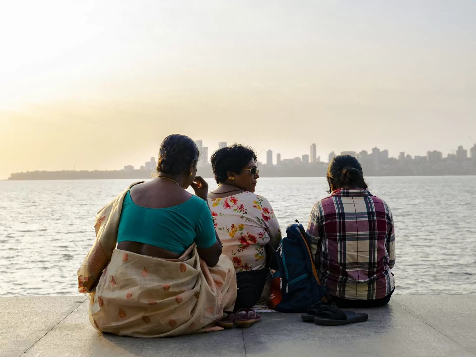Three women sit looking at the water along Marine Drive, Mumbai.