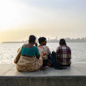 Three women sit looking at the water along Marine Drive, Mumbai.