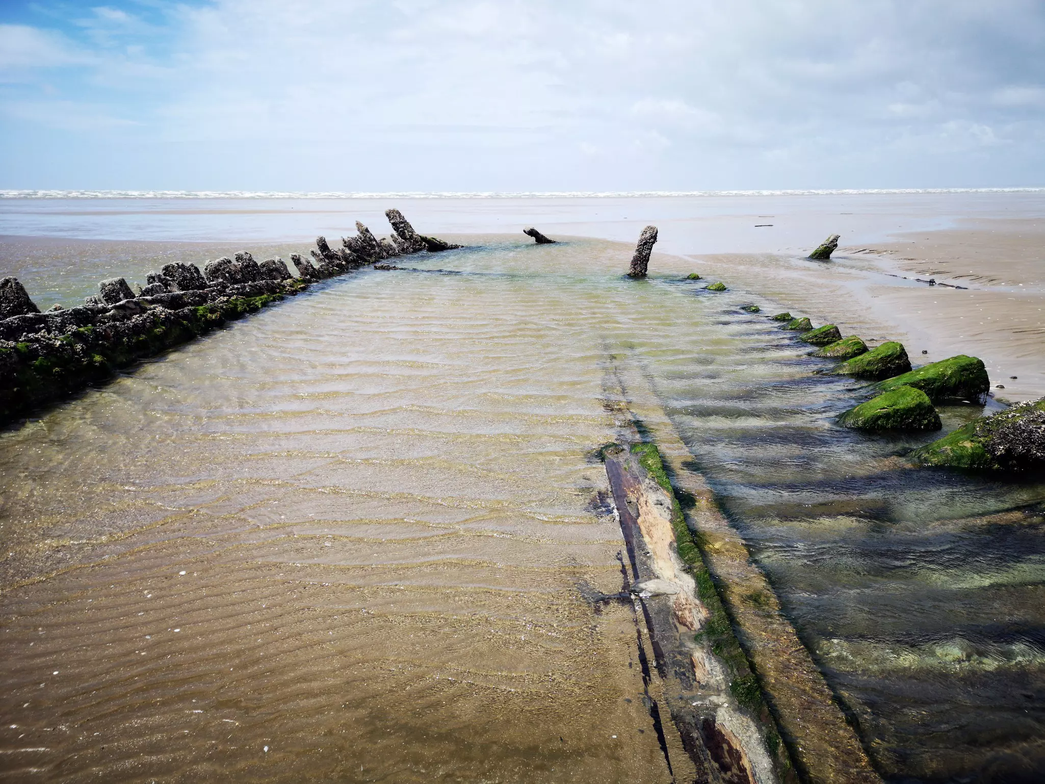 A rotting wooden hull of an ancient ship, wrecked on the sand.