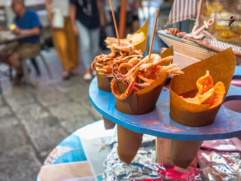 Fried seafood in brown paper cones sit on a blue rack.