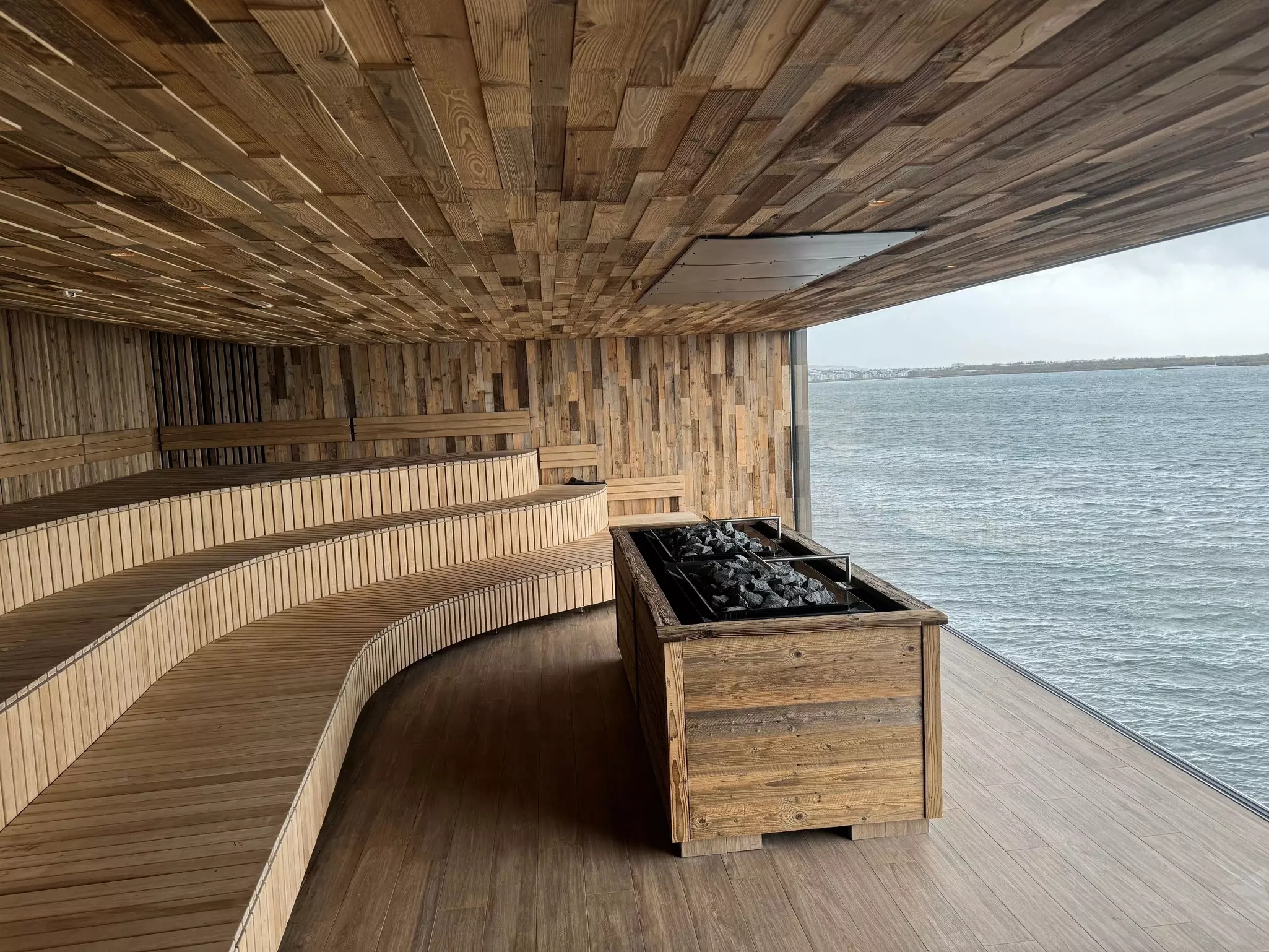 A large empty sauna has a huge window overlooking the sea.
