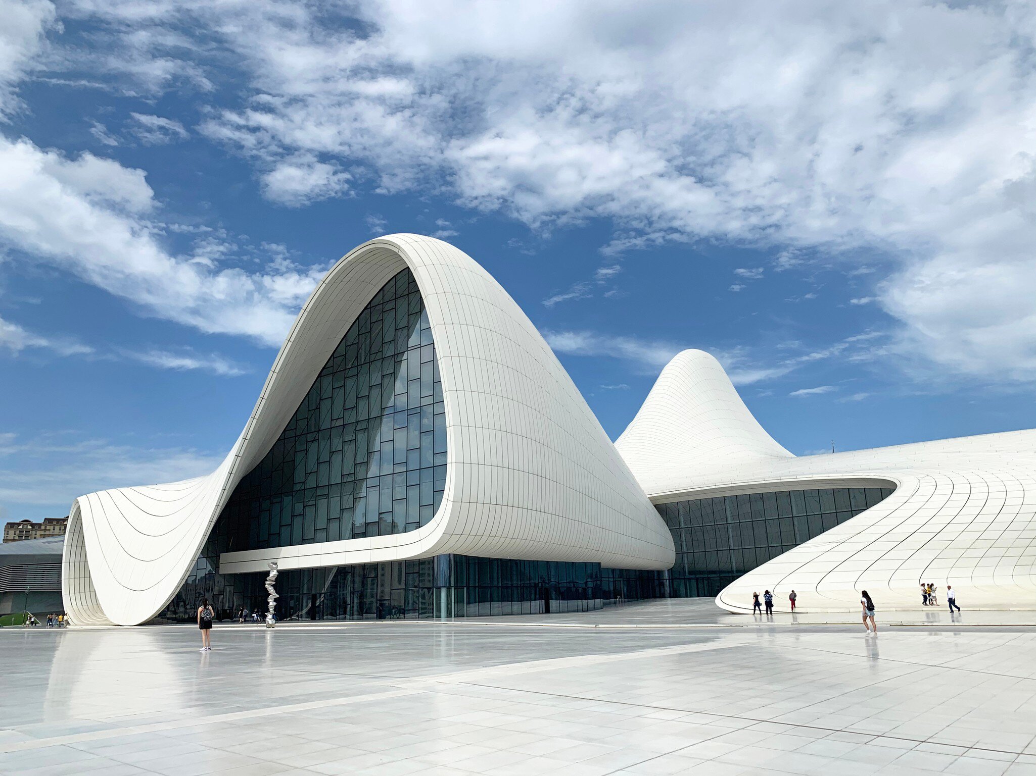 Wide exterior of Heydar Aliyev Center in Baku, Azerbaijan. Sillhouettes walking and blue sky.