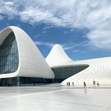 Wide exterior of Heydar Aliyev Center in Baku, Azerbaijan. Sillhouettes walking and blue sky.