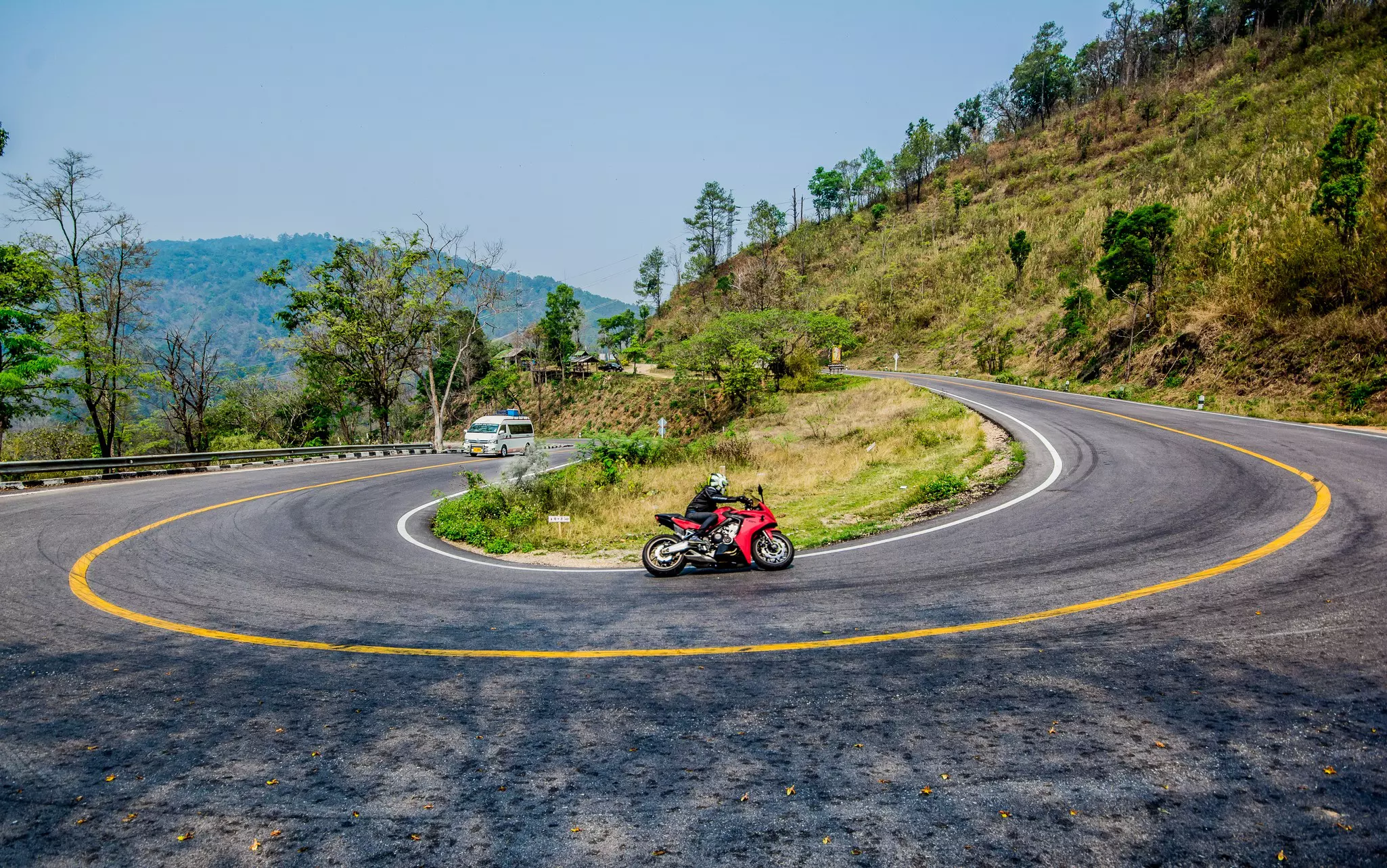 A motorcyclist turns around a tight bend in a mountain road