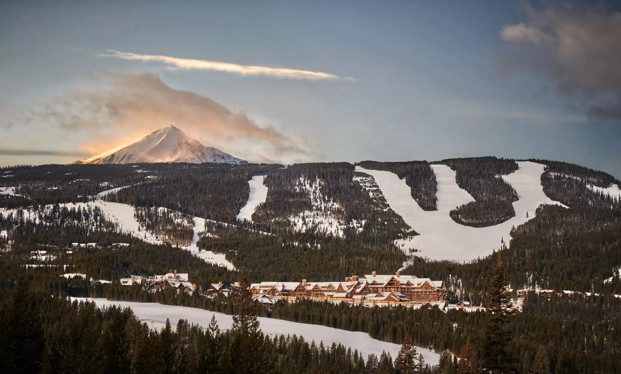 A tall mountain in the background. In the foreground a sprawled out ski resort with ski slopes surrounding it: Montage Big Sky resort in Montana