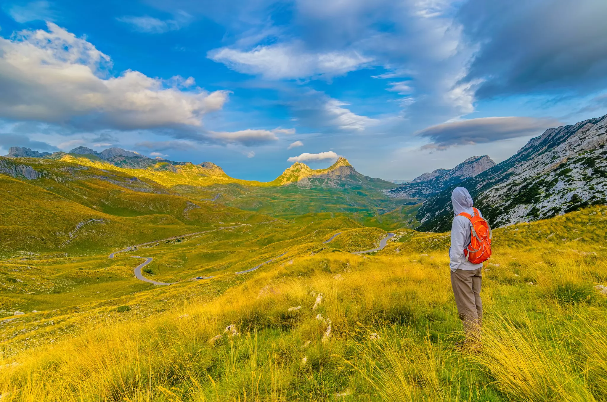 Traveler with backpack on a grassy path in the mountains in Durmitor National Park.