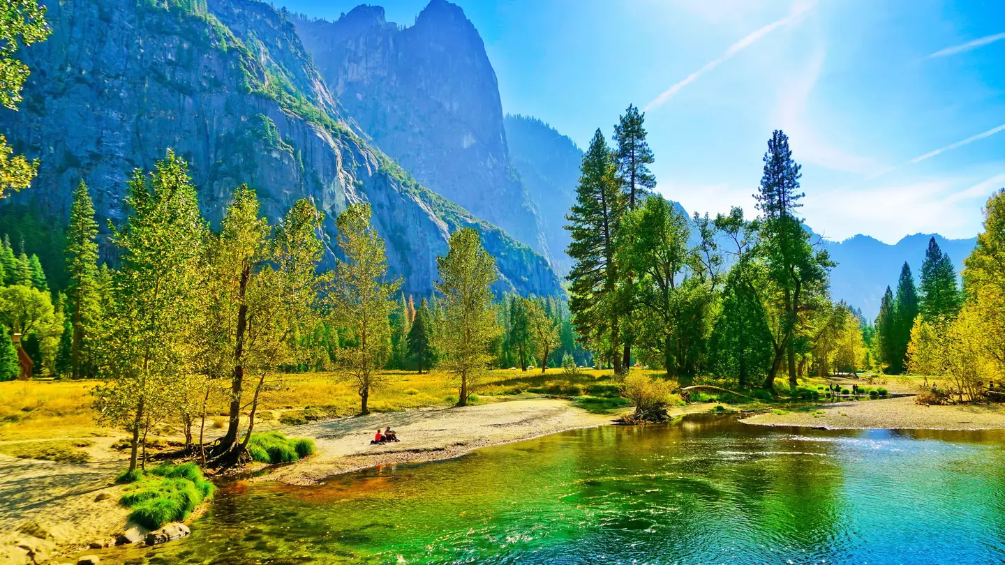 People sit on the banks of the Merced river in the Yosemite Valley during autumn.