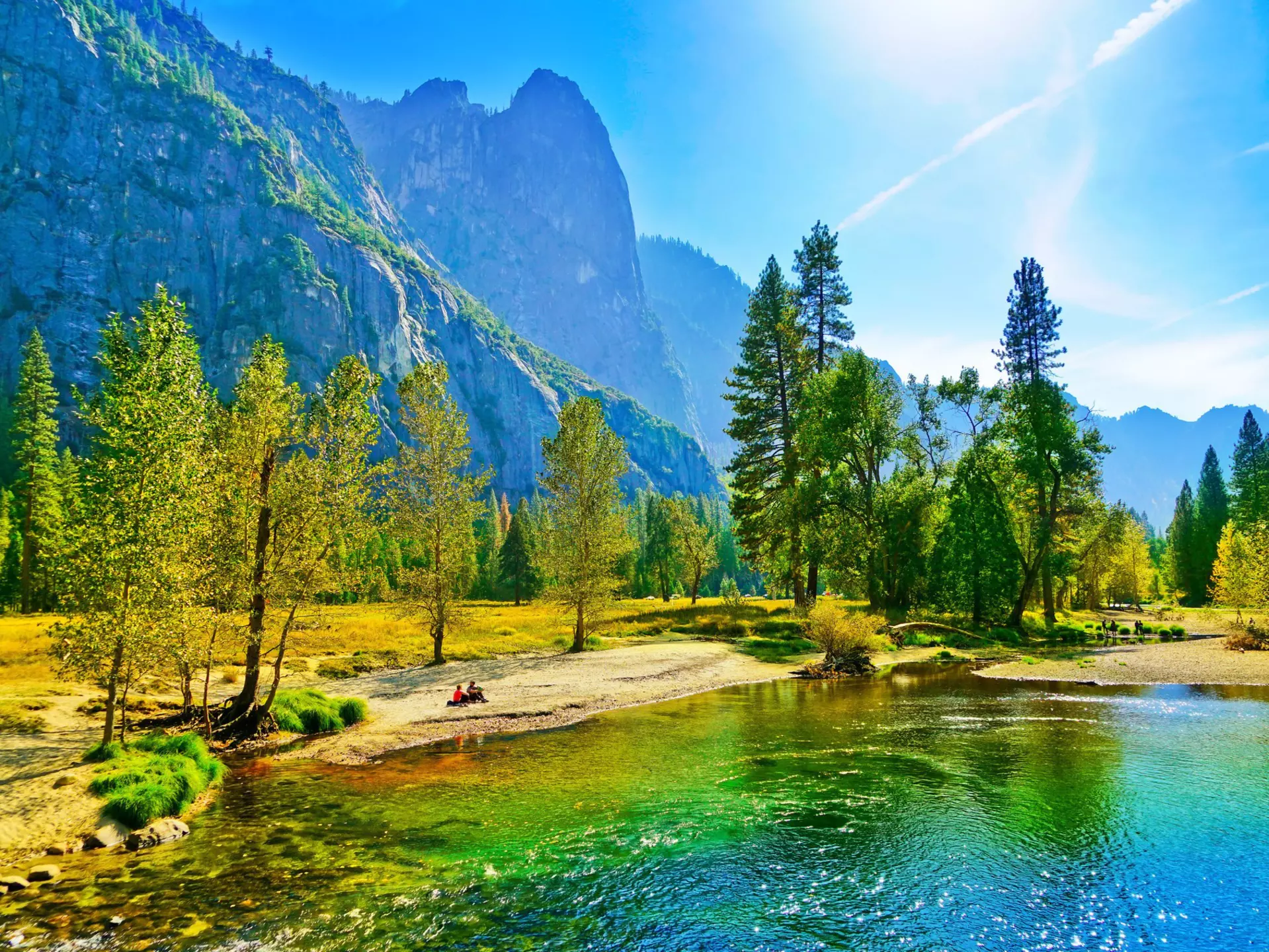 People sit on the banks of the Merced river in the Yosemite Valley during autumn.