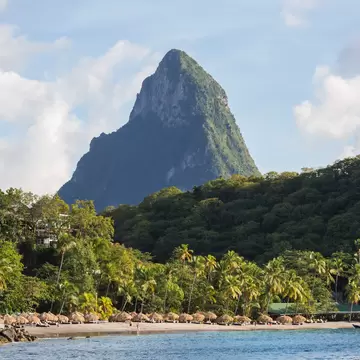 View across water to the palm-fringed beach of Anse Chastanet and steep rugged slopes of Petit Piton, evening, Soufrière, St Lucia, West Indies, North America