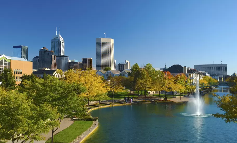 Indianapolis downtown towers rising behind the Central Canal, with a fountain, walkways and autumn trees in the foreground