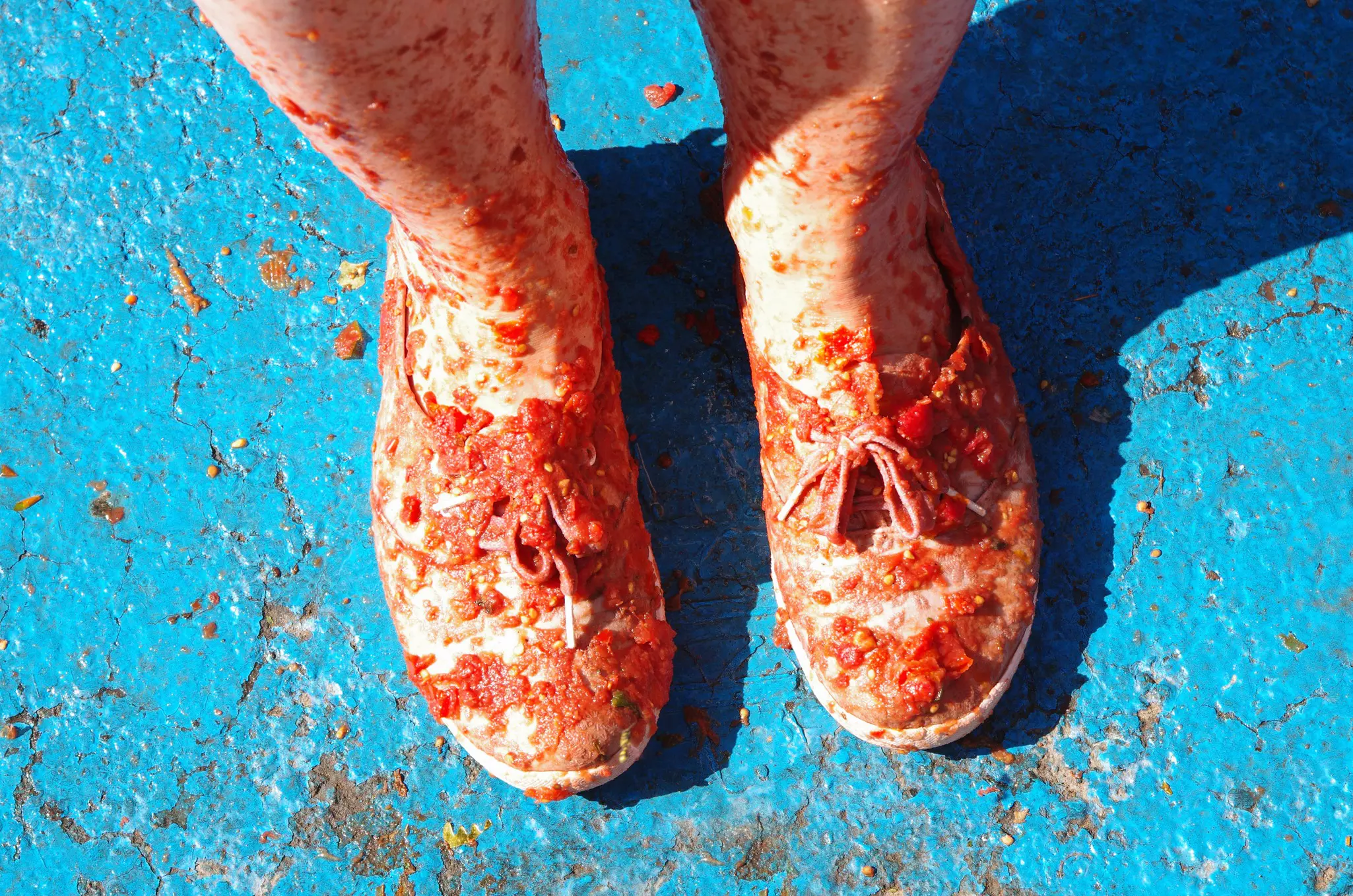 A human feet in shoes, covered with tomato slices on blue painted concrete ground