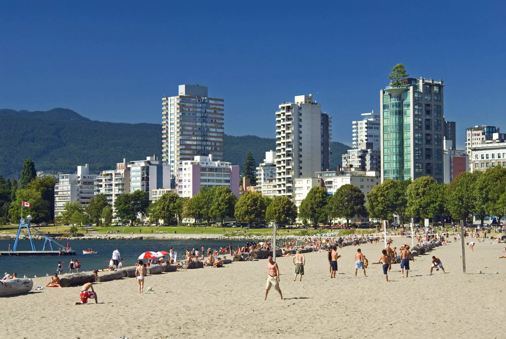 A city beach with people playing volleyball on a sunny day.