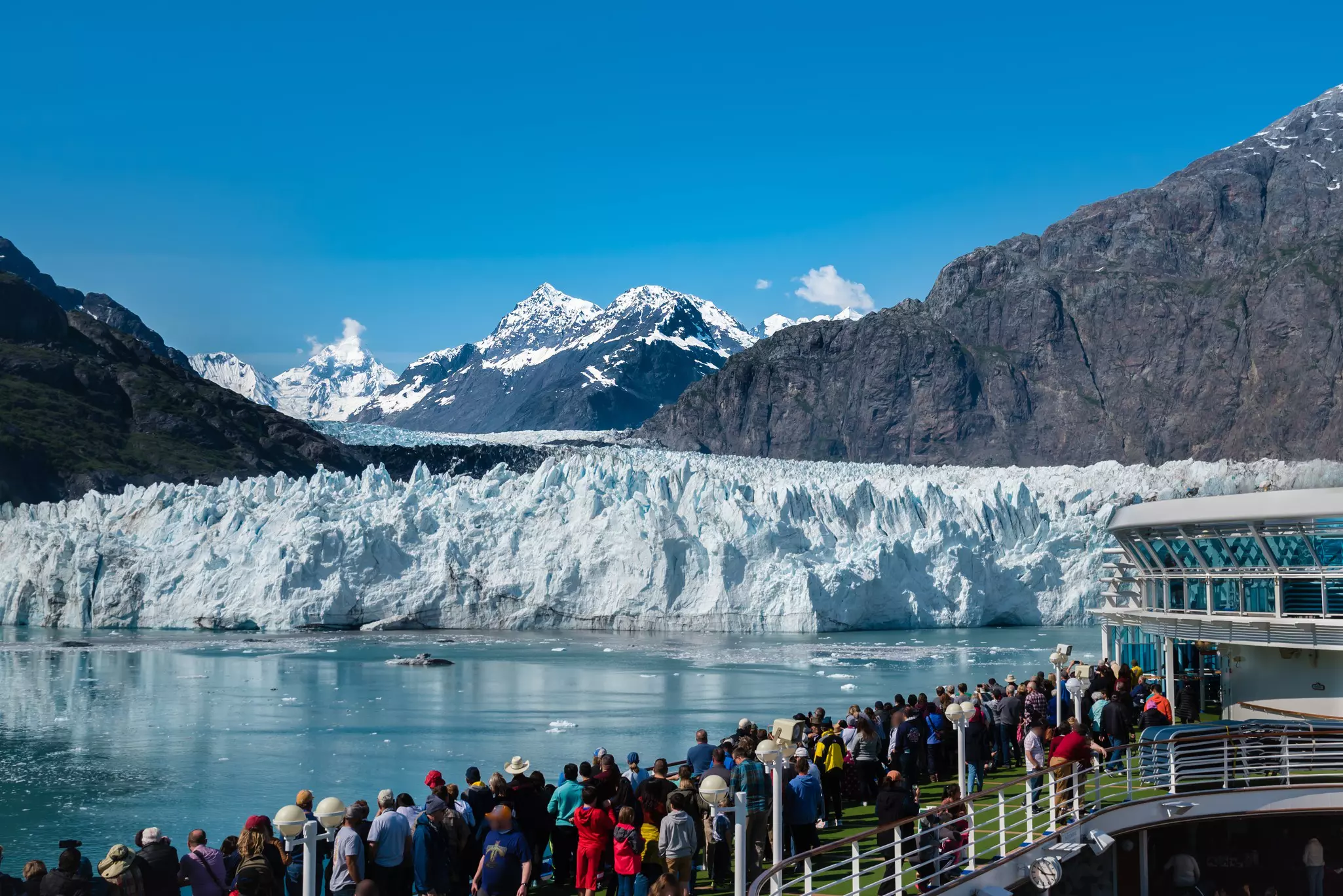 A group of tourists are enjoying the gorgeous view of the Margerie Glacier in the Glacier Bay of Alaska on a sunny day.