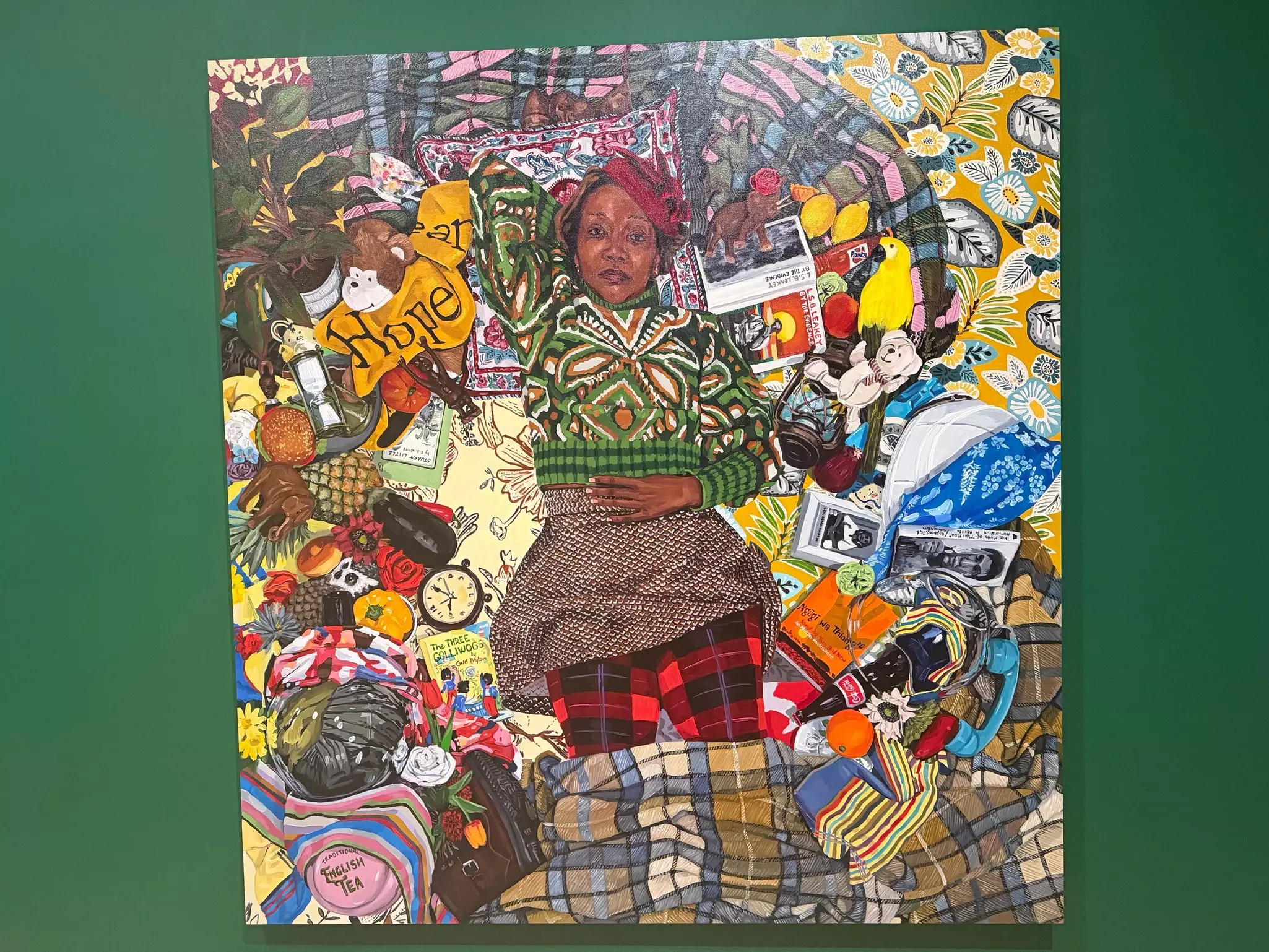 Photo of an oil canvas painting of woman in a color outfit laying on a colorful blanket surrounded by random items like clocks, plants, fruit and books.